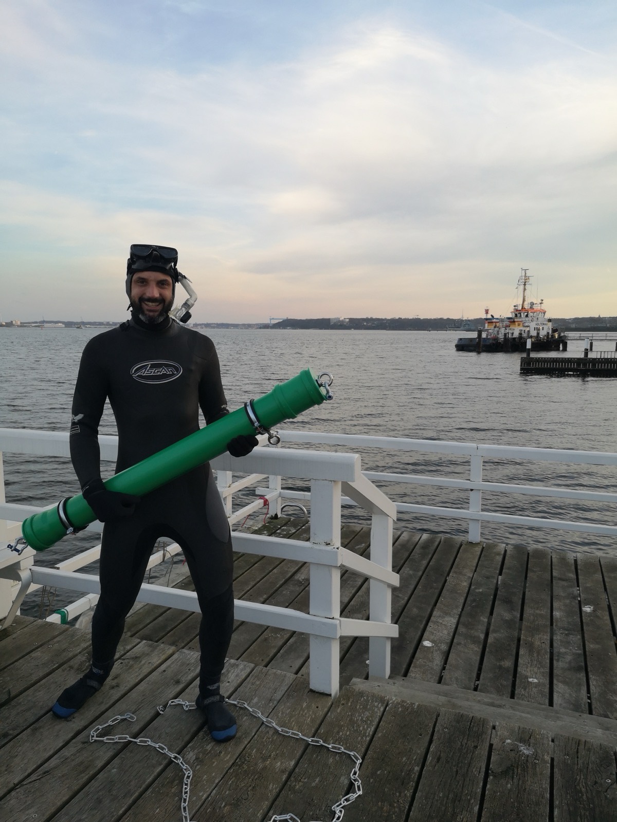 Team member in a wetsuit on a jetty, holding a HYDRA mooring strut before a dive